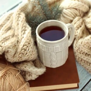Mug of coffee sitting on a book next to knitting supplies.