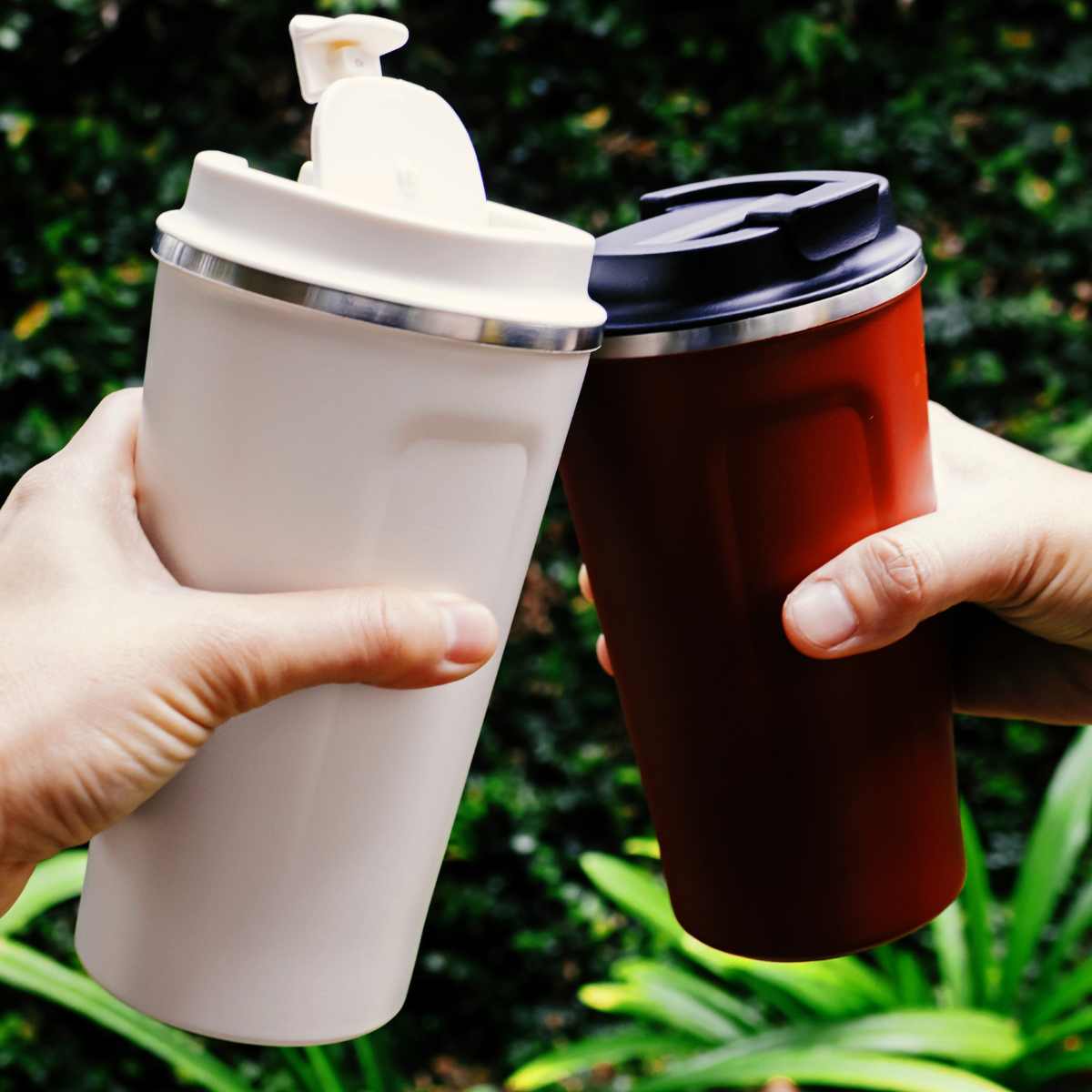 Two hands clinking thermal mugs of coffee.