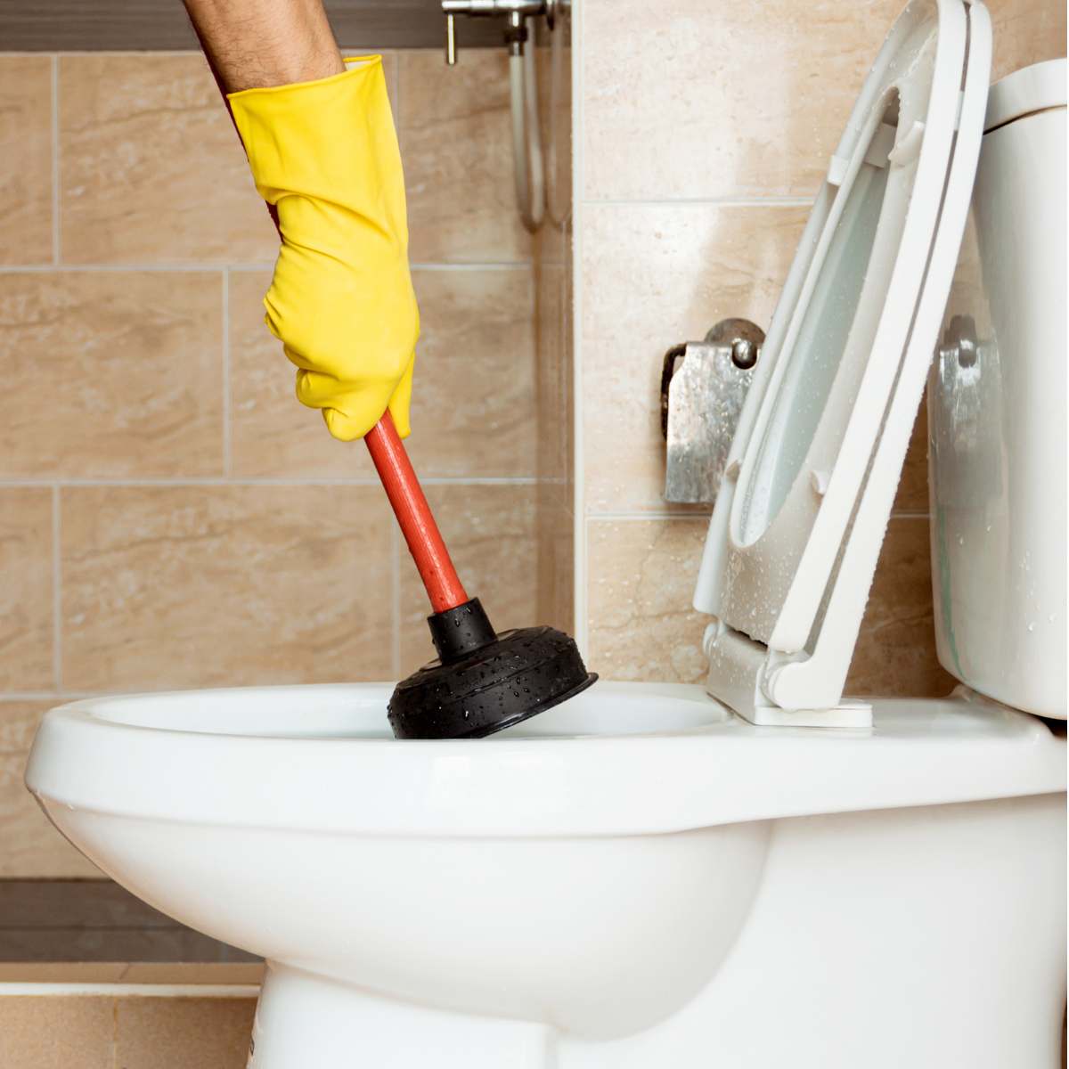 Hand holding a toilet plunger in a toilet.