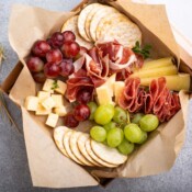 Mini individual charcuterie box full of crackers, cheese, meat and fruit.