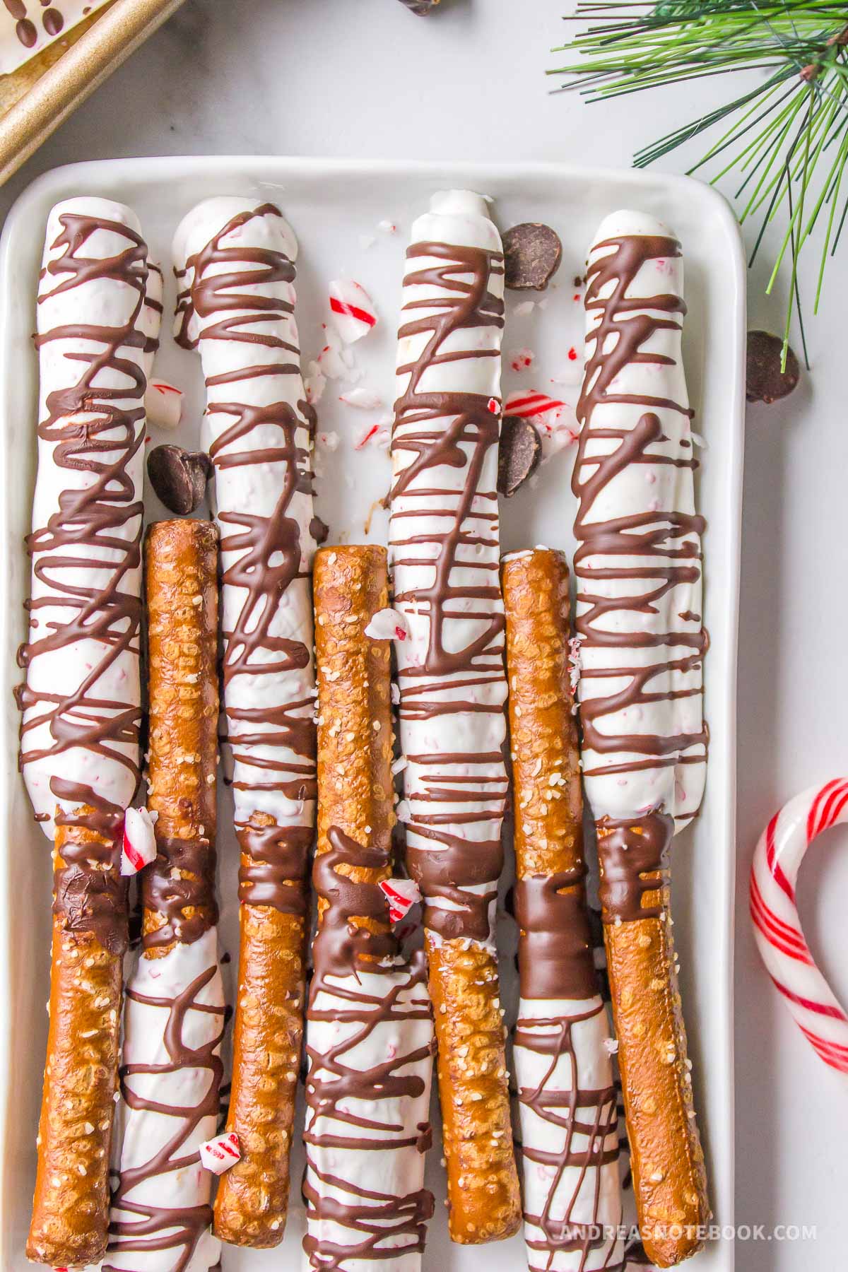 White chocolate and dark chocolate peppermint candy covered pretzel rods on a baking sheet for Christmas.