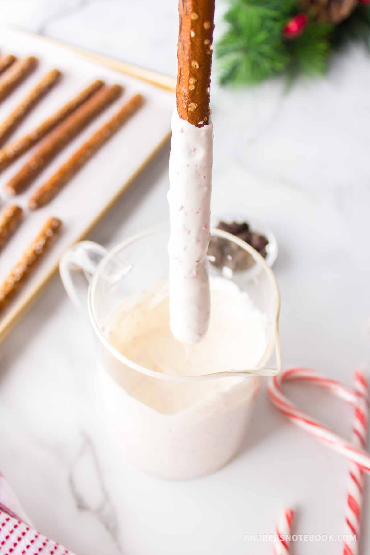 White chocolate peppermint candy melted in a glass measuring cup with a pretzel rod dipped in.