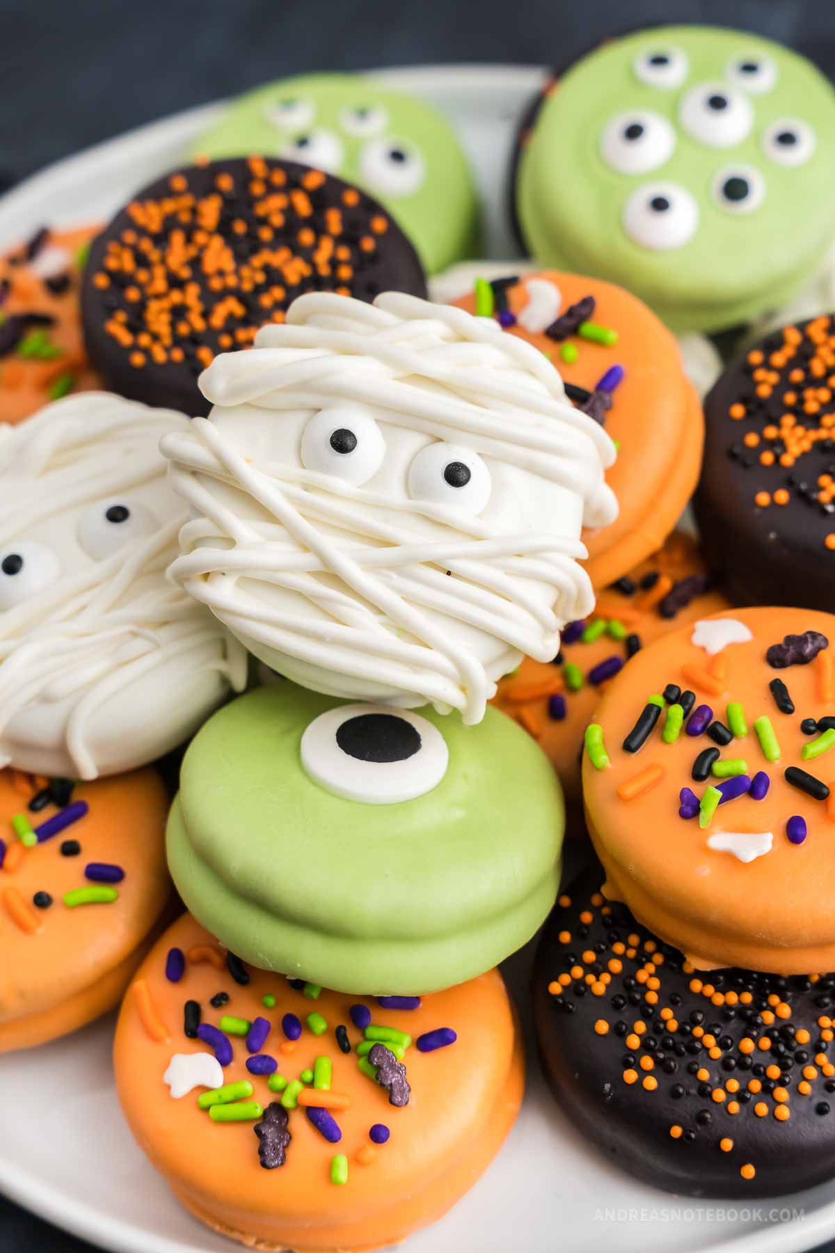 Plate full of cute and spooky chocolate dipped oreos including a mummy, monster and sprinkled.