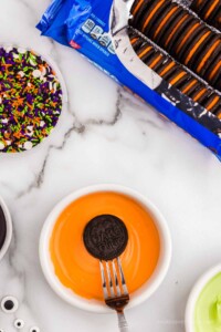 Oreo being dipped into orange candy melts.