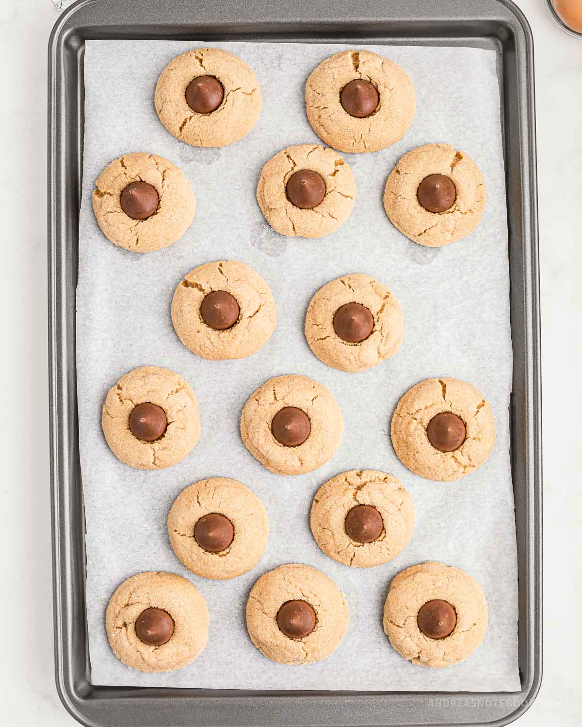 Hershey kiss placed on baked peanut butter cookies on baking sheet.