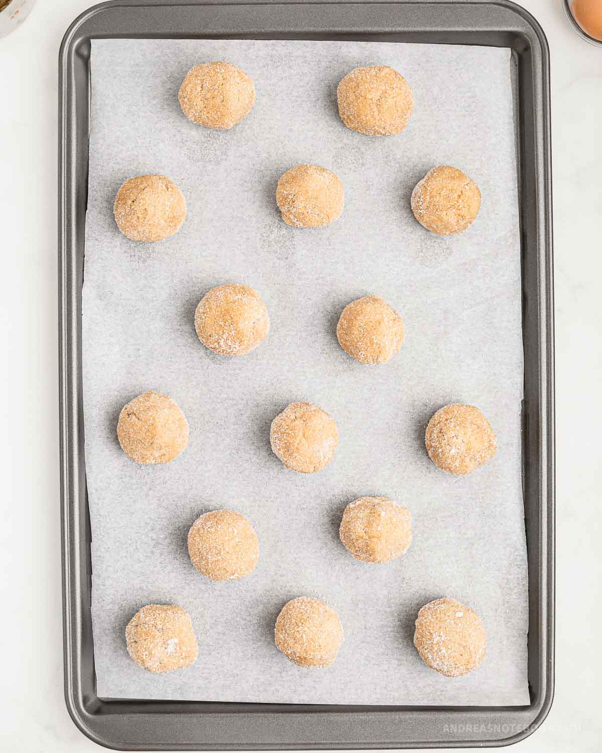 Cookie balls rolled in sugar on a baking sheet.