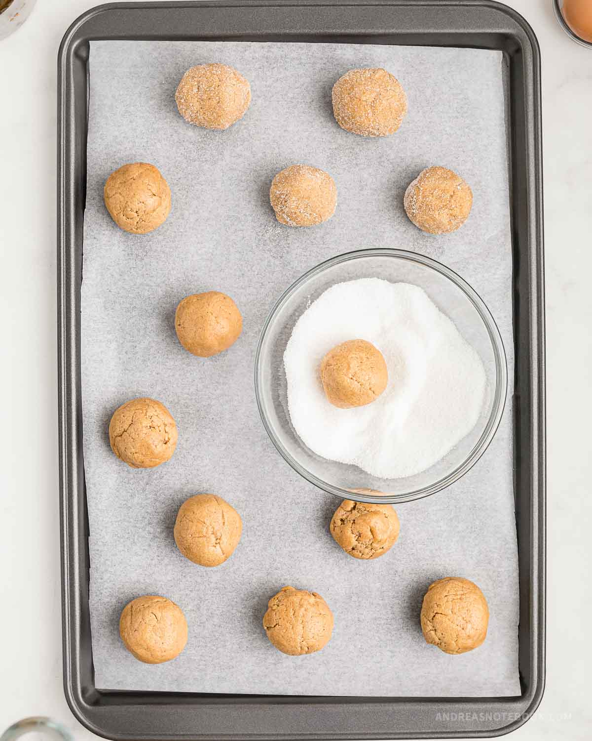 Ball of peanut butter cookie being rolled in sugar.