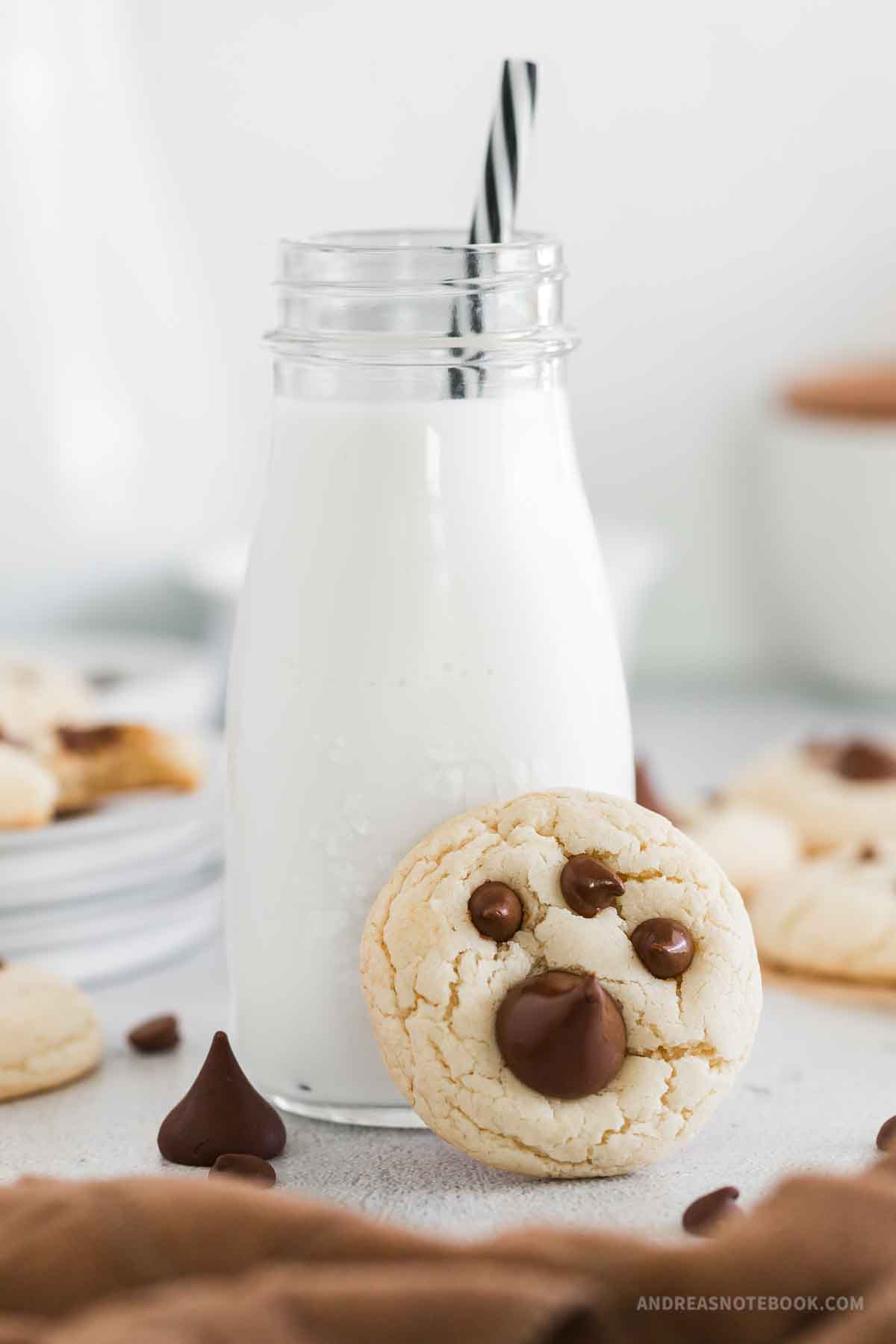 Glass bottle of milk with paper straw and a paw print cookie propped up against it.