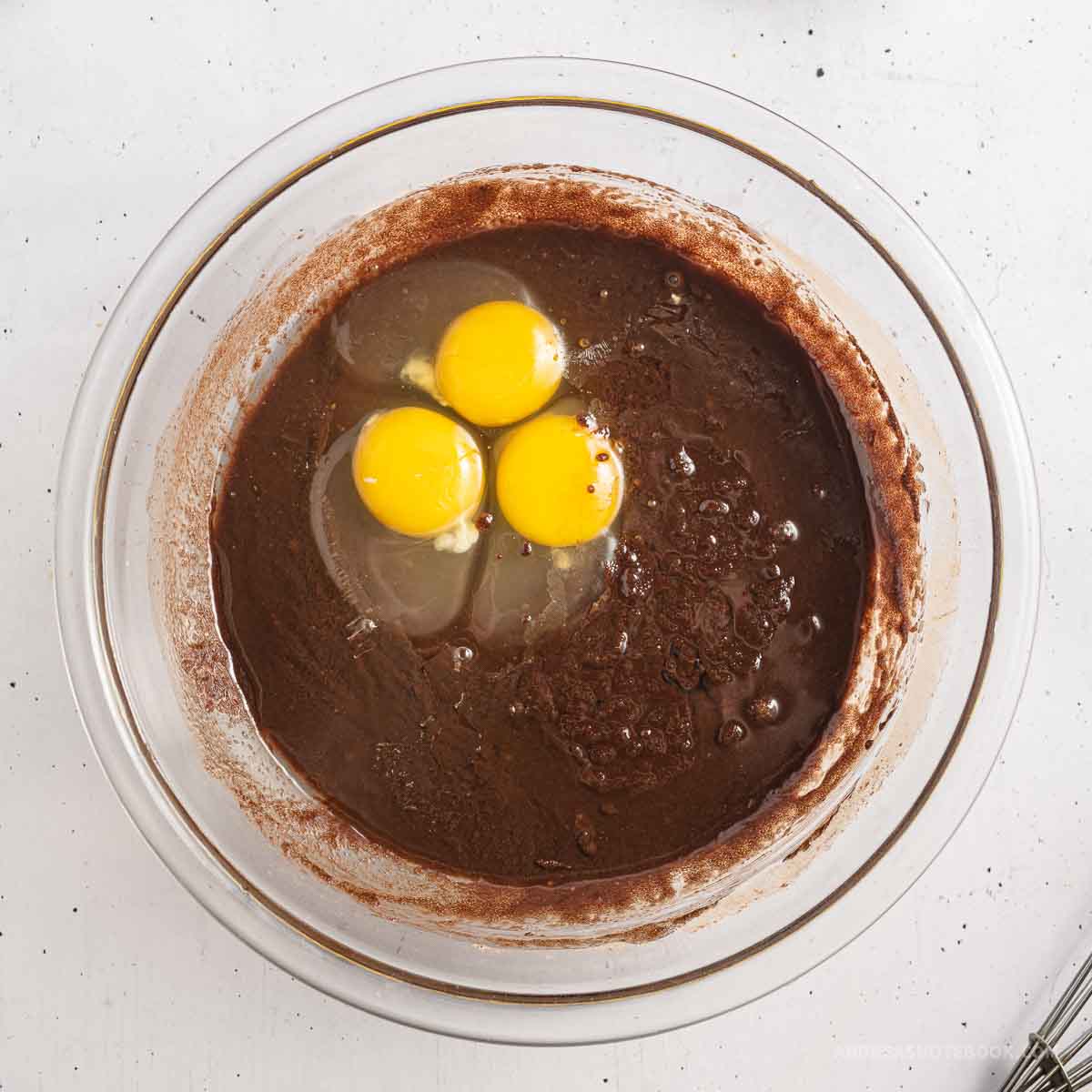 Bowl full of melted chocolate and butter mixture with eggs cracked on top.