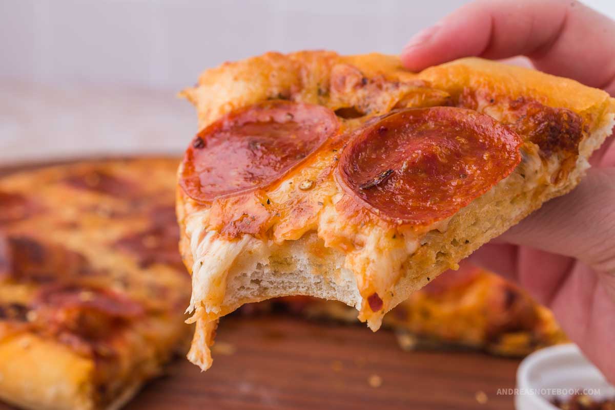 Bite out of a slice of pepperoni deep dish pizza.