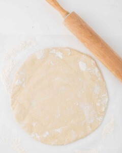 Pizza dough rolled out with a rolling pin to make a large circle.