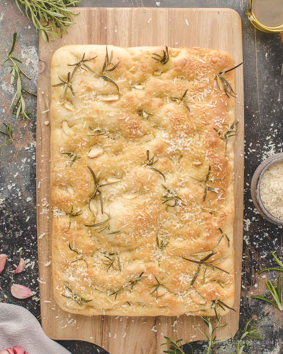 Cooked golden brown focaccia bread on a bread board.