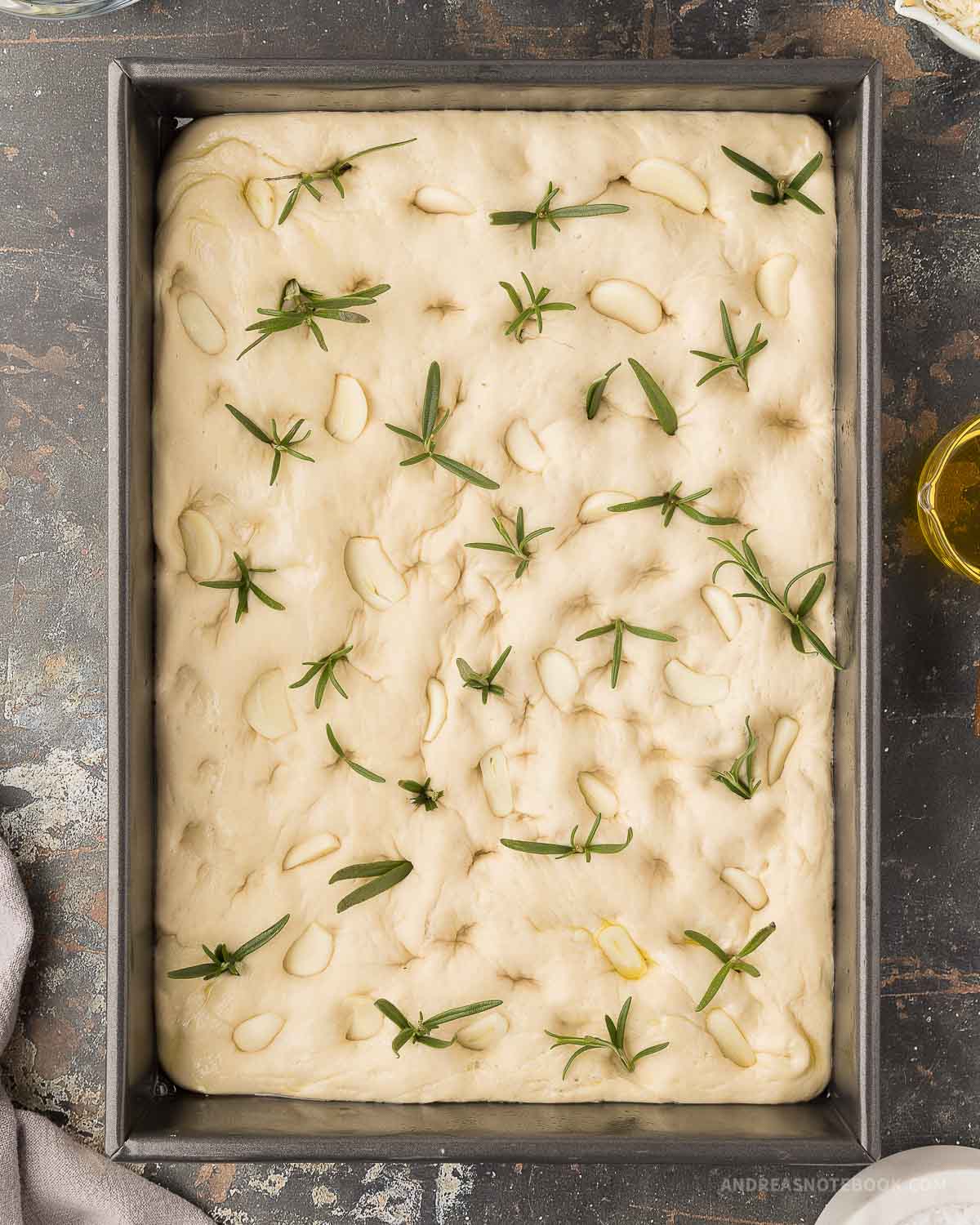 Garlic and rosemary on top of raw focaccia bread dough.