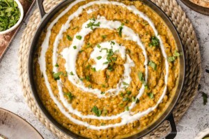 Cooked red lentil curry dal with a swirl of white yogurt and cilantro garnish on top.