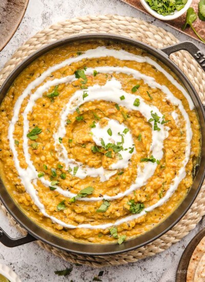 Large pan of cooked red lentil dal with swirl of yogurt on top.