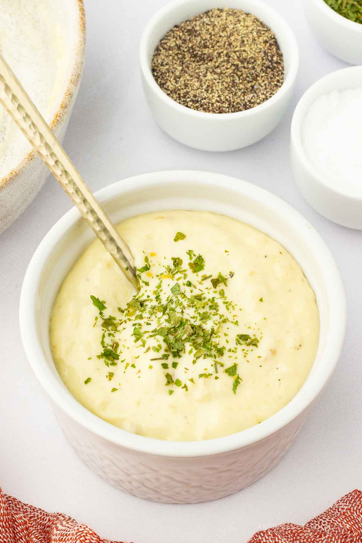 Bowl of lemon garlic aioli with a spoon in it and herbs on top.