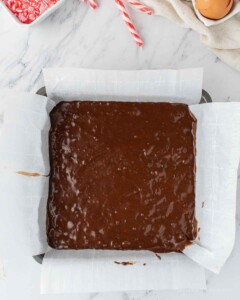 Brownie batter poured into square baking pan lined with parchment paper.
