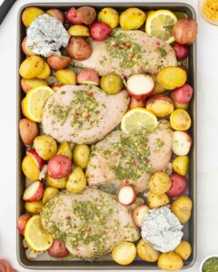Sheet pan full of raw chicken and potatoes.