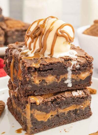 Stack of two layered biscoff butter cookie brownies with a scoop of vanilla ice cream and caramel sauce on top.