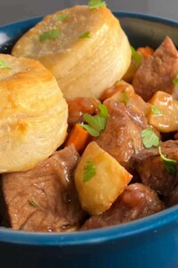 Bowl of beef and potato stew with two golden biscuits sitting on top.