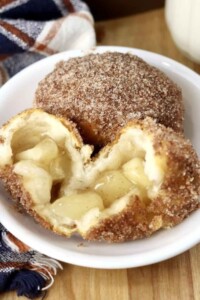 Two cinnamon covered cooked balls of dough, one opened with apple pie filling inside.