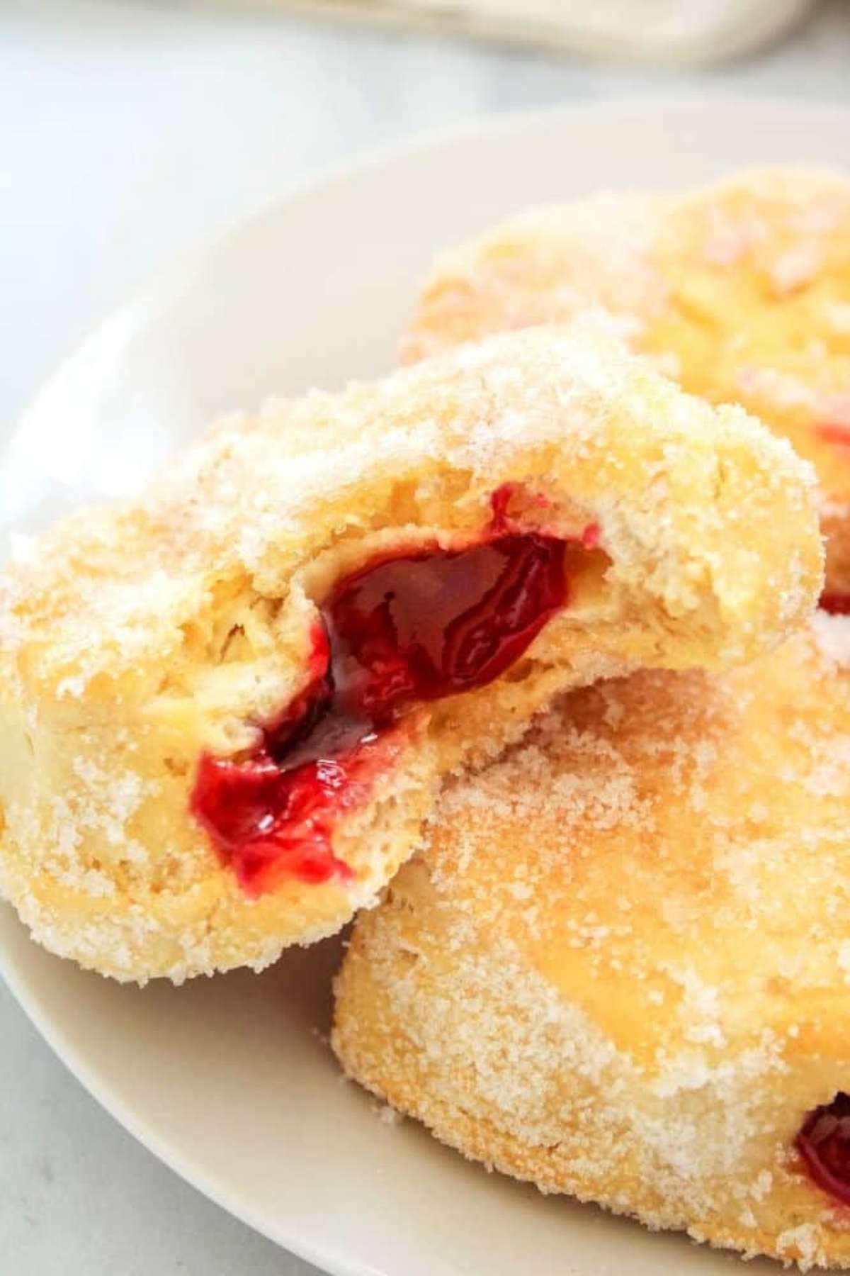 Jelly stuffed donut on a plate with a bite taken out of the donut.