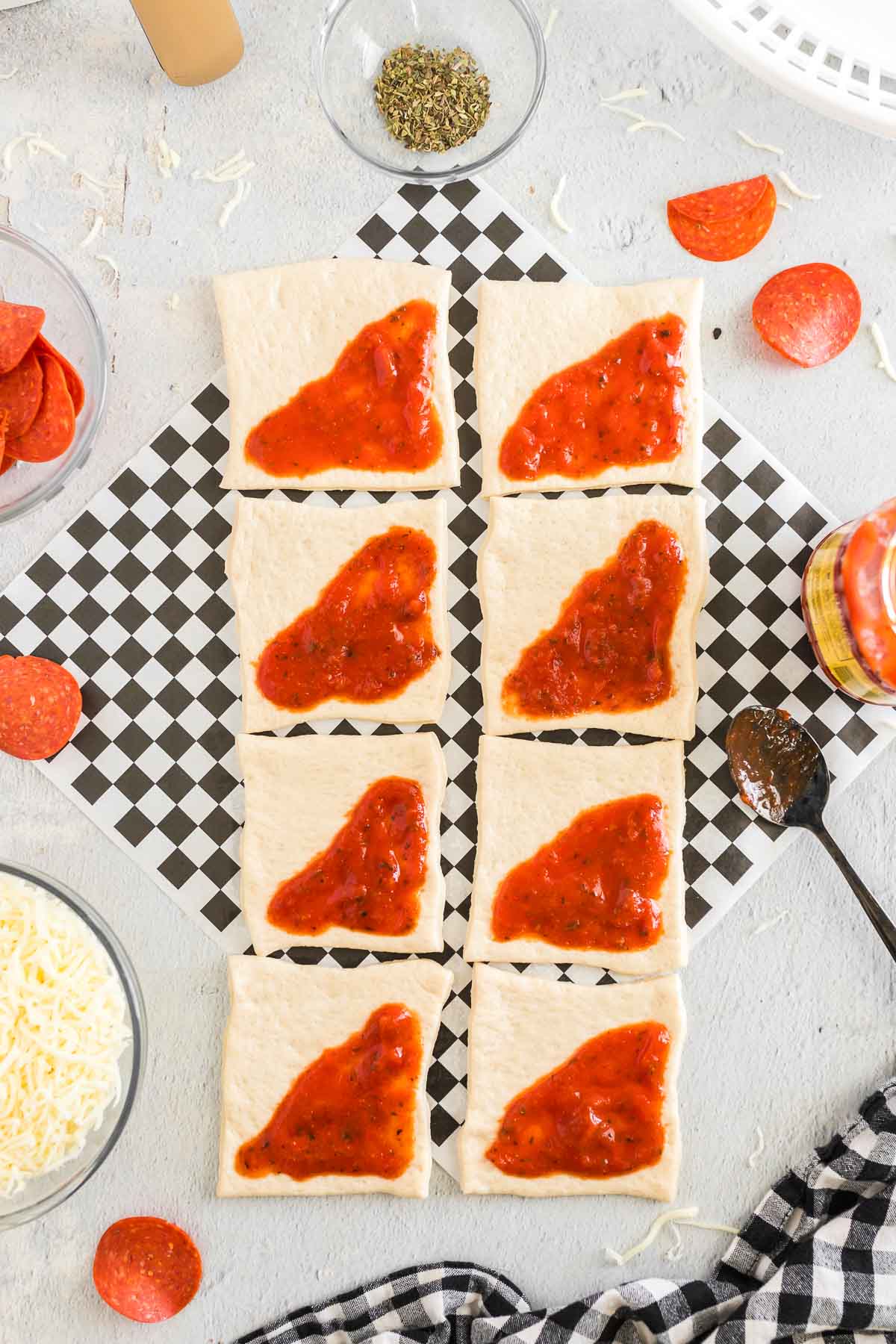 Spoonful of sauce spread onto one triangle half of each pizza dough square.