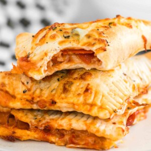 Stack of 3 homemade air fryer cooked pepperoni hot pockets (pizza pockets) with top one having a bite out of it and cheese showing through.