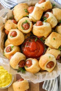 Plate full of mini pigs in a blanket around a bowl of ketchup.