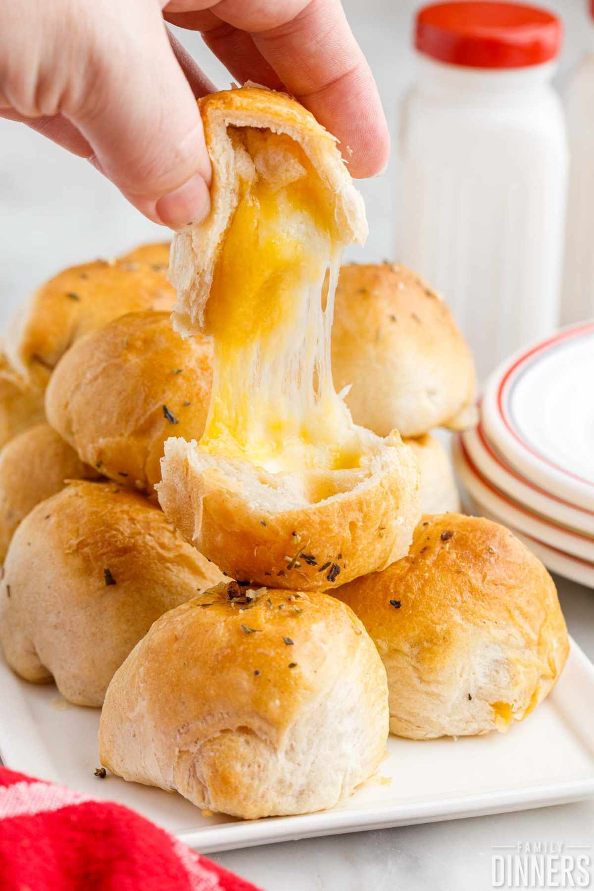 Hand holding an opened 3 cheese biscuit bomb with melted cheese pulling out.
