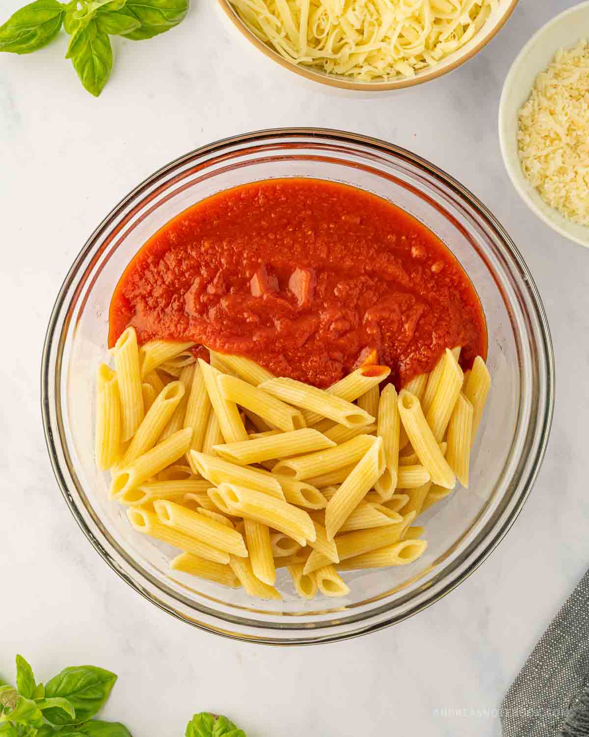 Marinara sauce mixed with penne pasta in a bowl.