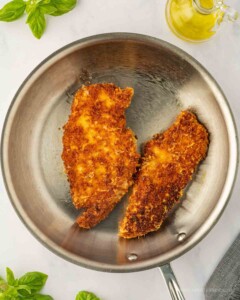 Skillet with cooked parmesan crusted chicken breasts.