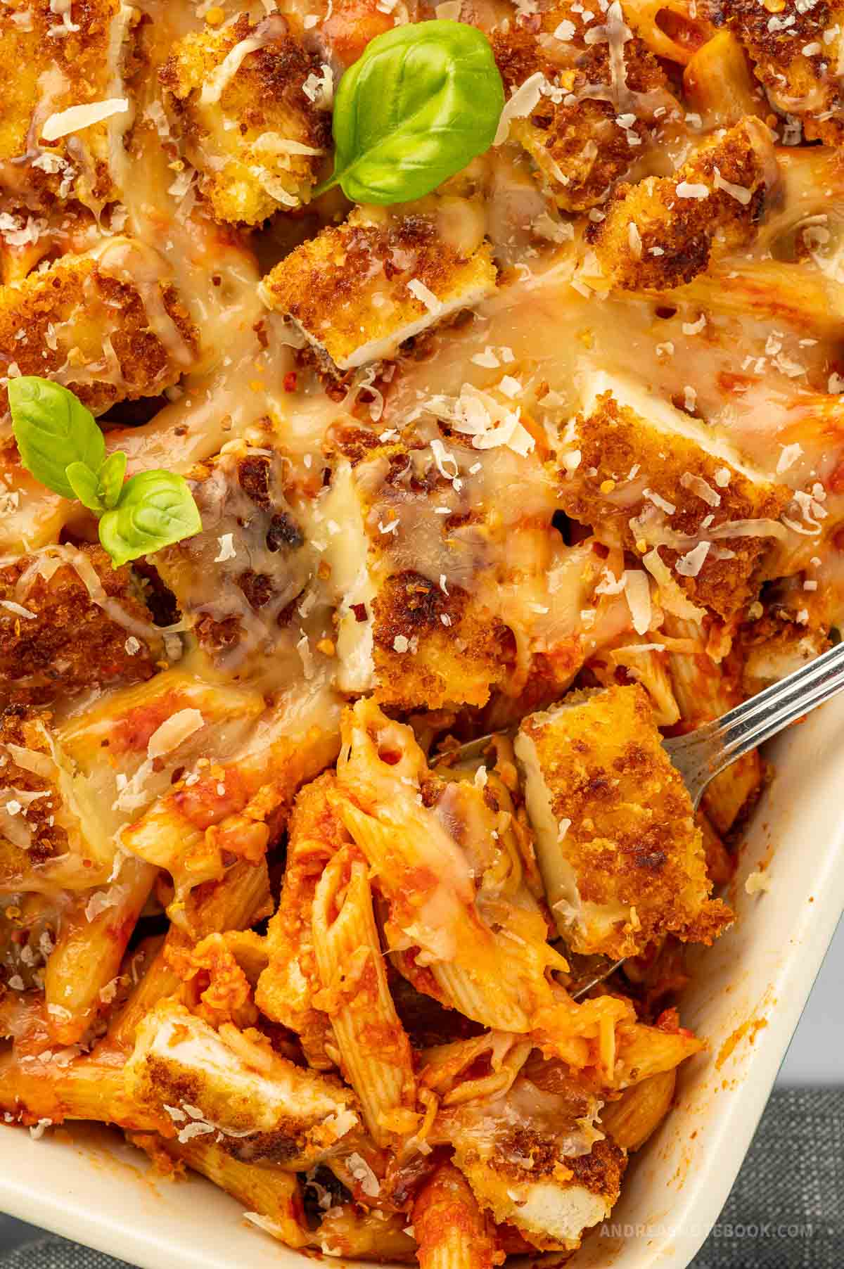 Casserole dish with baked chicken parmesan and penne pasta.