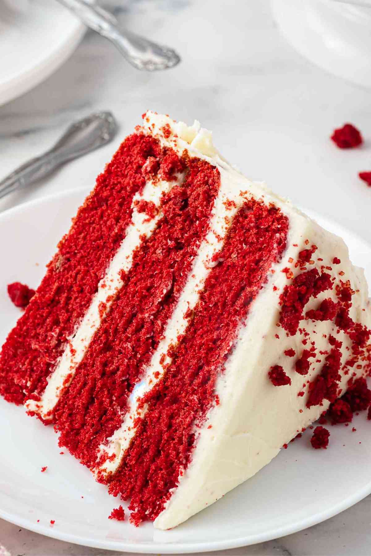 Large wedge slice of layered red velvet cake with white frosting.