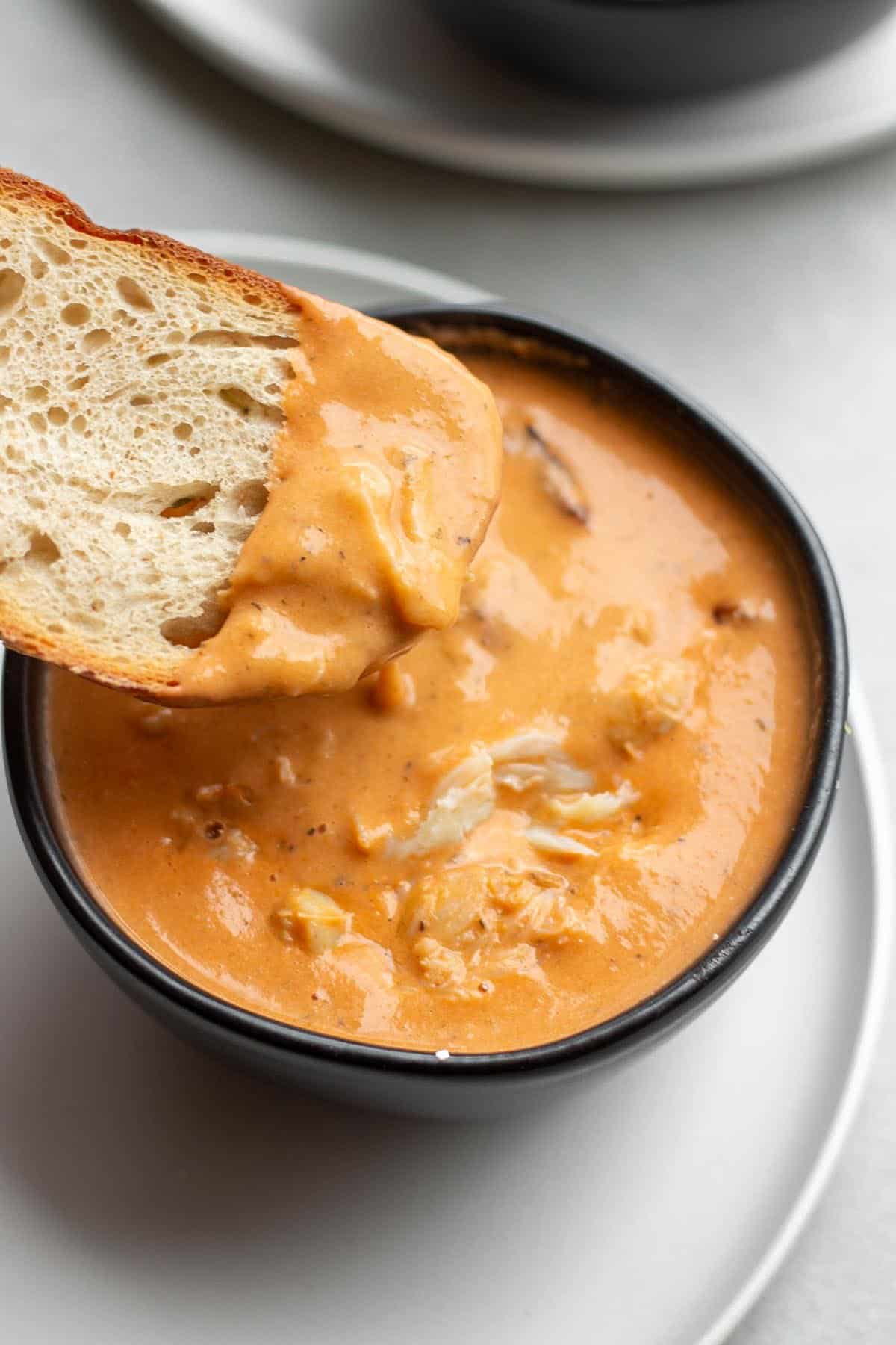 Bowl of creamy crab bisque soup with crusty bread being dipped in.