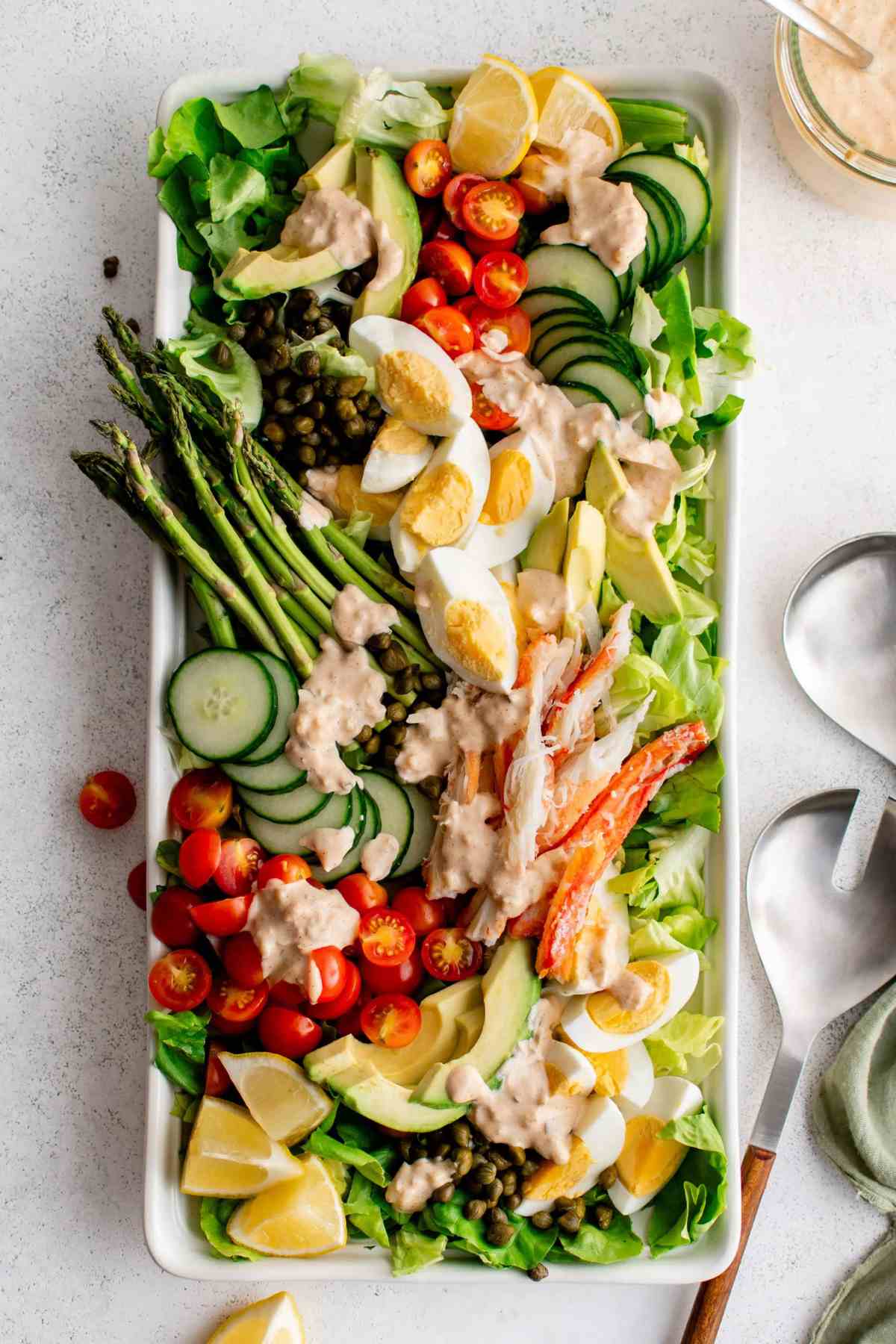 Rectangular platter with deconstructed crab louie salad with asparagus, tomatoes, avocado, lettuce, crab meat and more.
