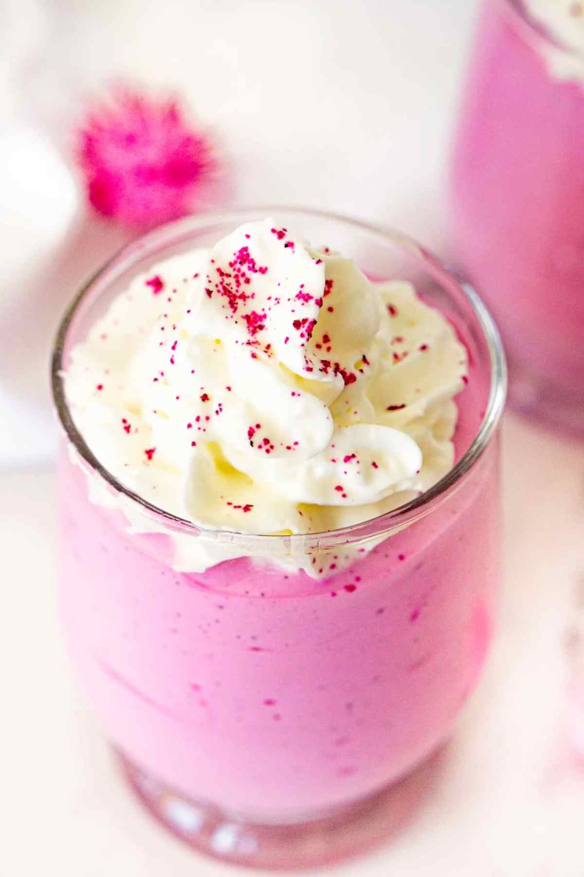 Fuschia colored dragon fruit whipped cottage cheese in a glass topped with whipped cream.