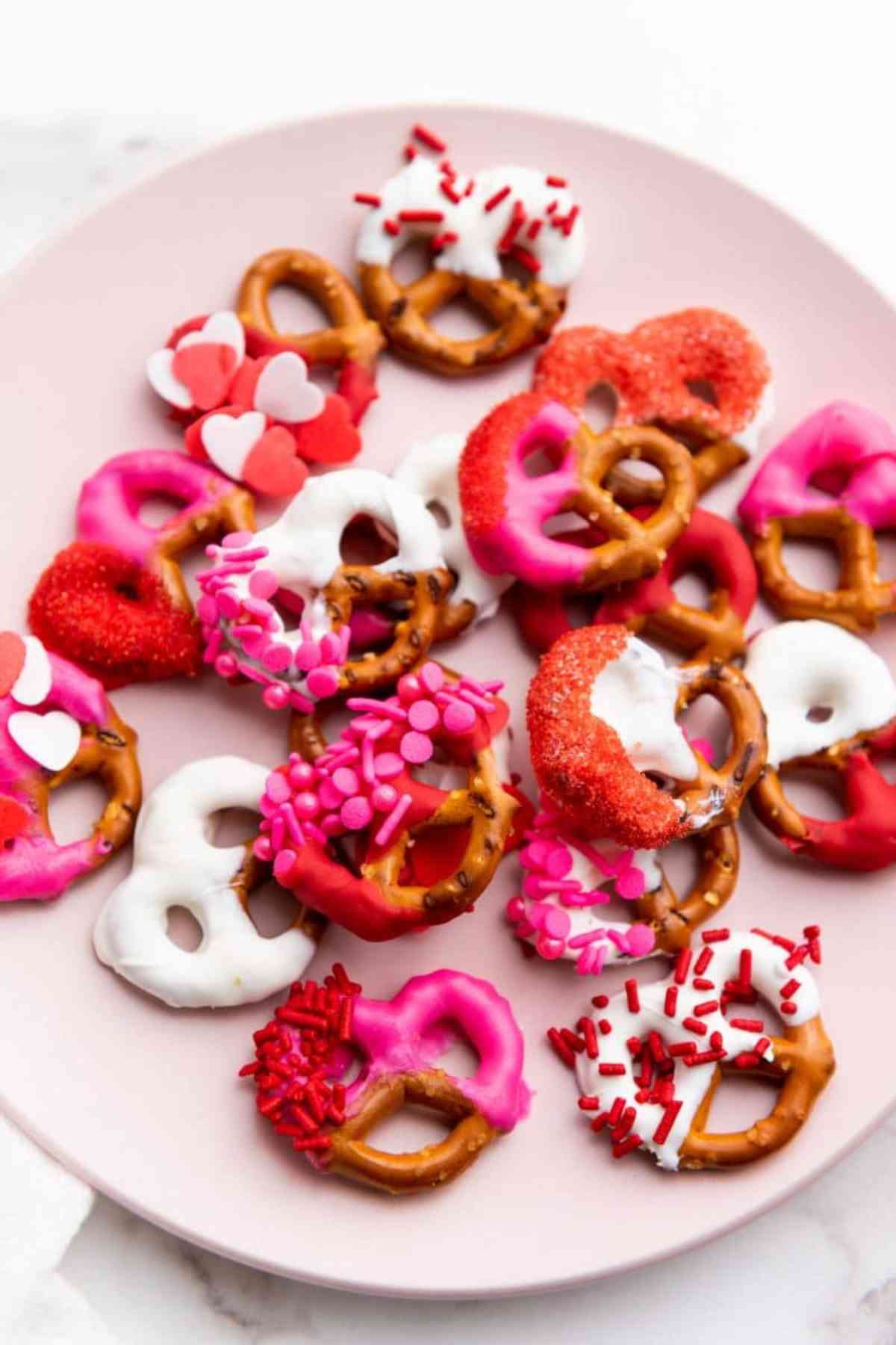 Pile of pretzels on a plate. Pretzels are decorated with pink and white chocolate and sprinkles.
