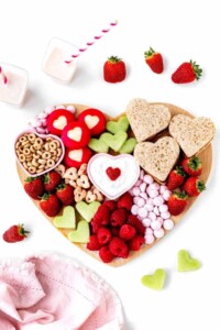 Heart shaped charcuterie board full of heart shaped fruits, cookies, treats and including fresh fruit, cheerios and more.