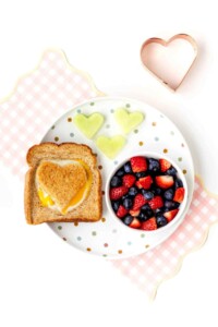 Toast on a plate with an egg cooked inside and a bowl of berries next to it.