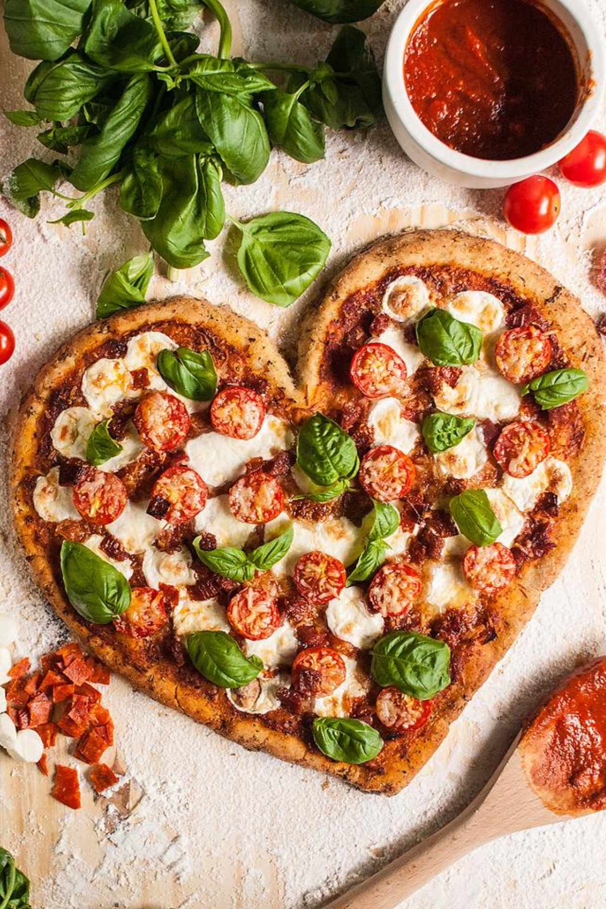 Heart shaped gluten free pizza with homemade gluten free pizza crust topped with cheese, basil leaves and cherry tomatoes.
