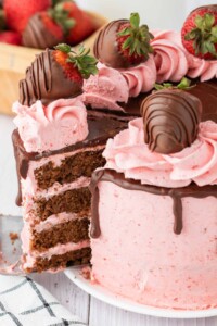 4 layers of chocolate cake with strawberry frosting between layers and around the cake is topped with chocolate covered strawberries.