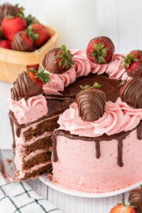 Round 4 layered chocolate cake with pink strawberry frosting topped with chocolate covered strawberries.