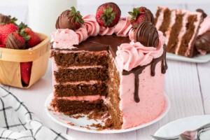 4 layer chocolate cake with strawberry frosting topped with chocolate covered strawberries.