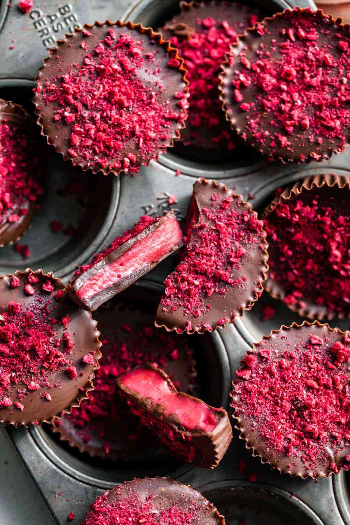 Pile of raspberry cream filled chocolate candy cups topped with raspberry colored sprinkles.