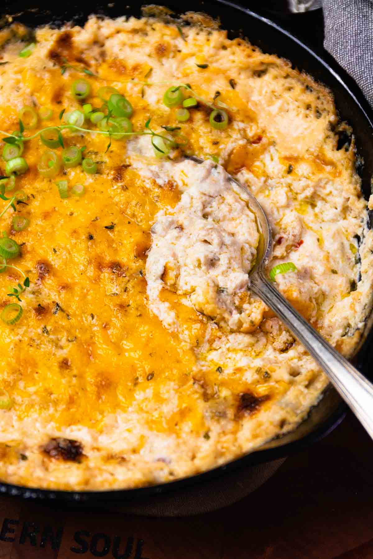 Cast iron skillet full of cheesy baked crab dip with spoon scooping out a spoonful.