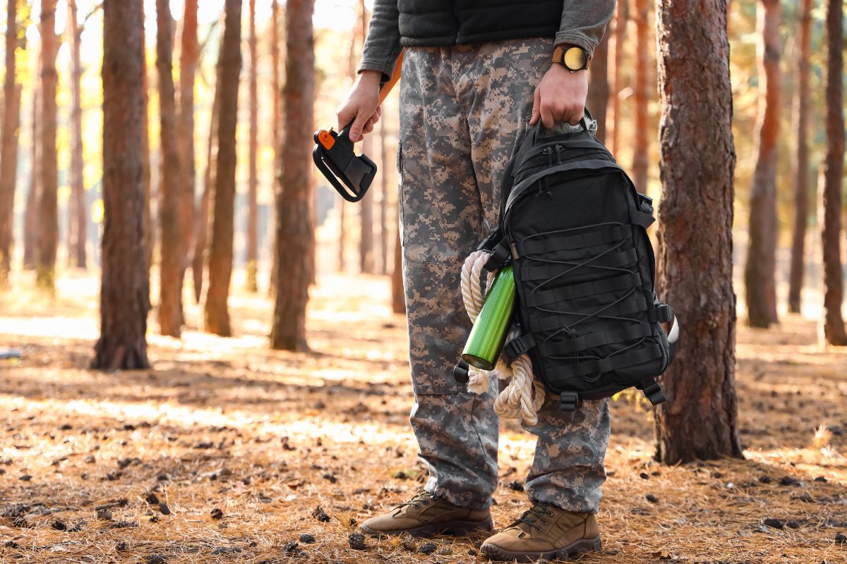 Man holding a zombie survival backpack with water bottle and rope hanging off side.