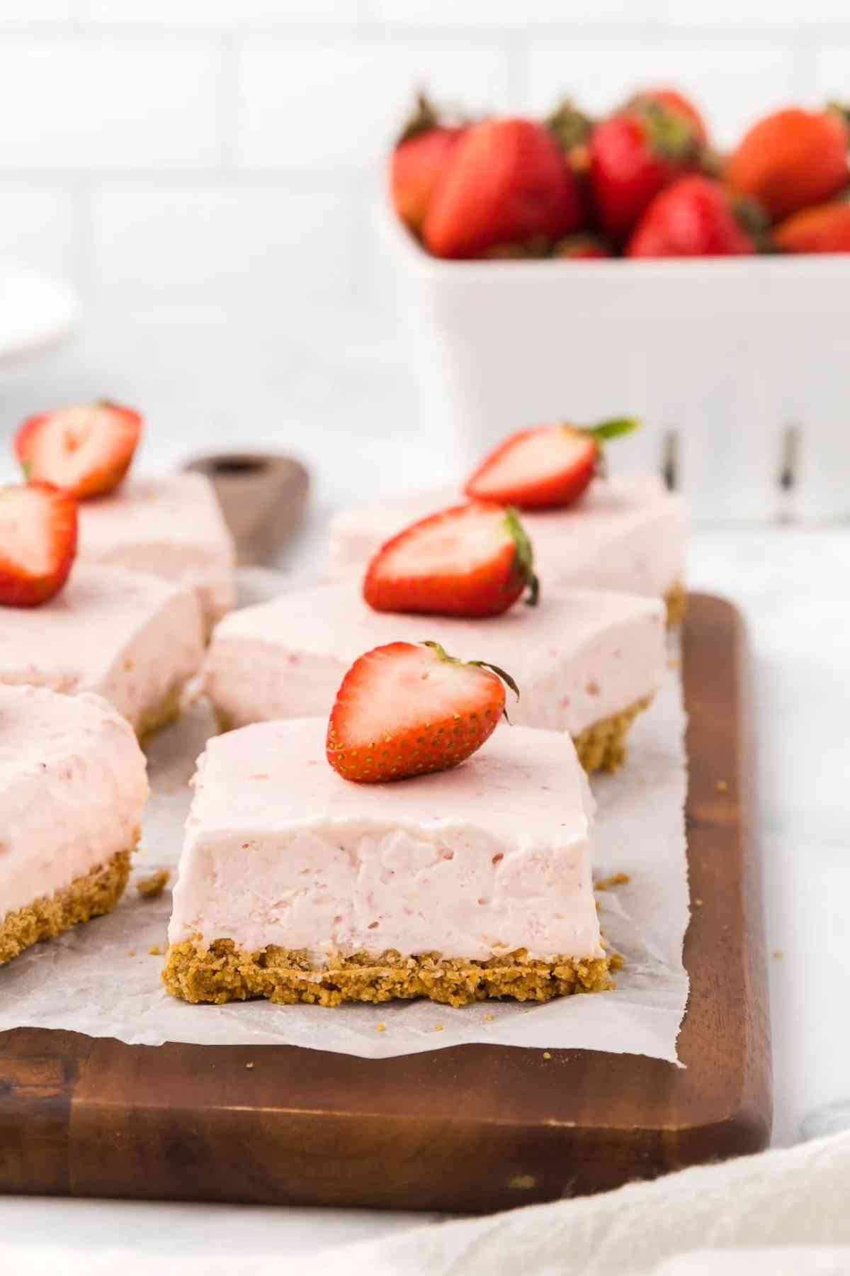 6 squares of no bake strawberry cheesecake bars topped with a half strawberry.