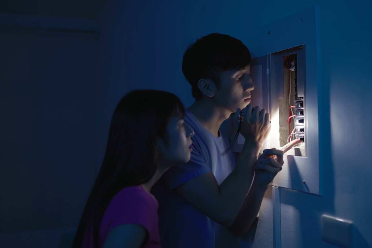 Two people with a flashlight looking at an electrical panel.