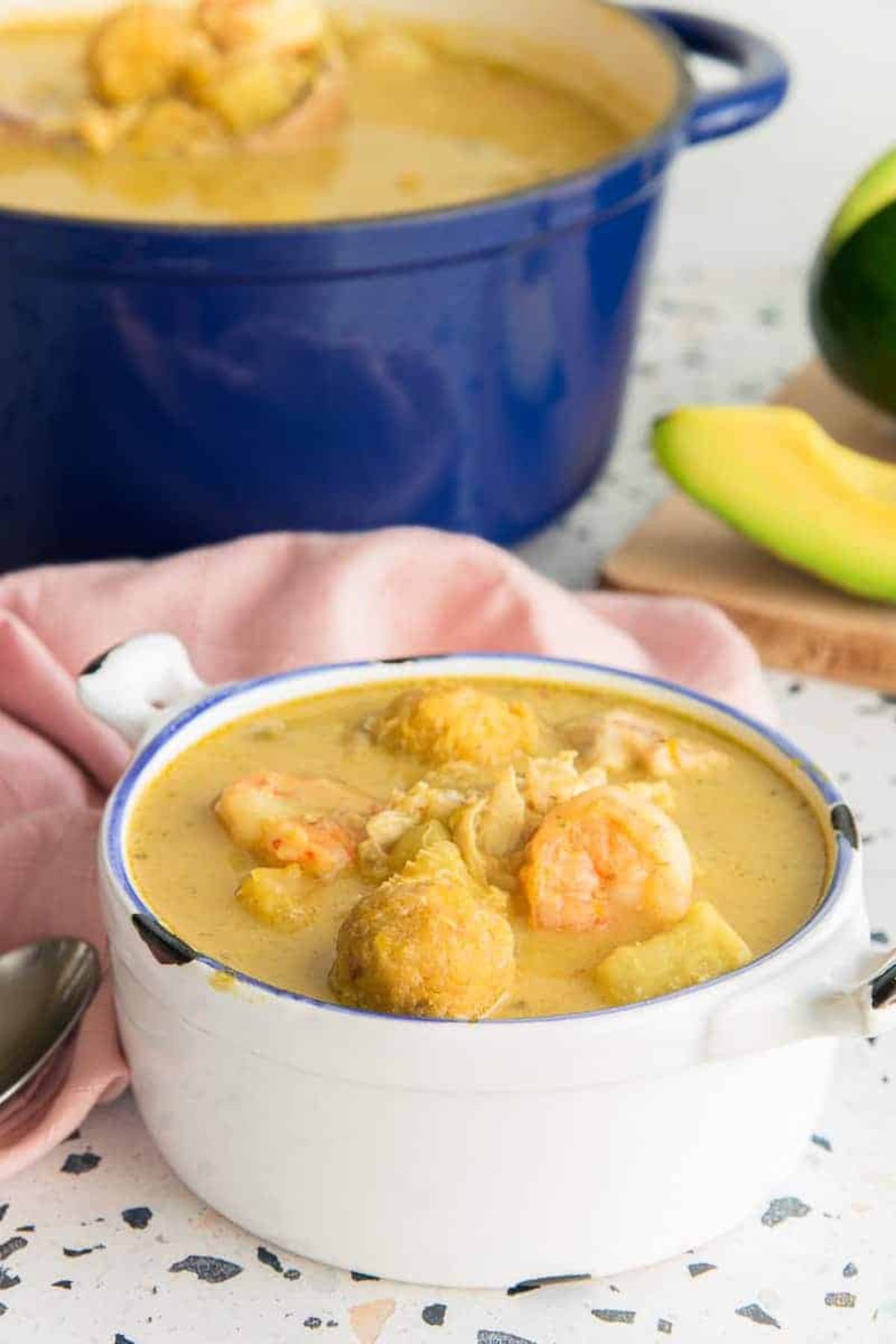 Bowl of creamy puerto rican coconut seafood stew in front of a dutch oven of soup.